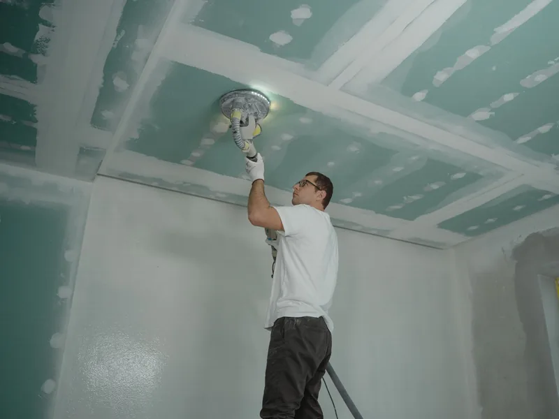 A drywall finisher sanding a taped and mudded ceiling with a pole sander