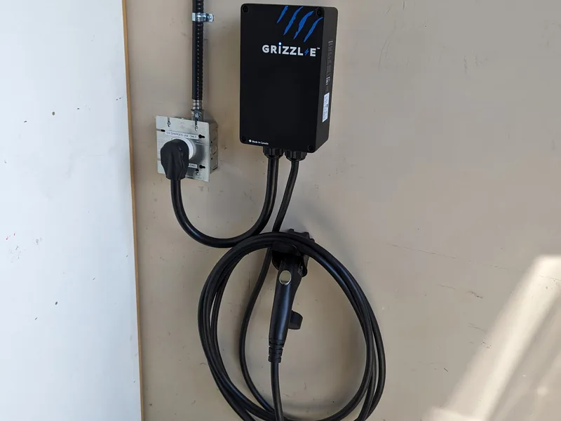 A wall-mounted electric vehicle charger with its cable coiled beside it, wired to a junction box